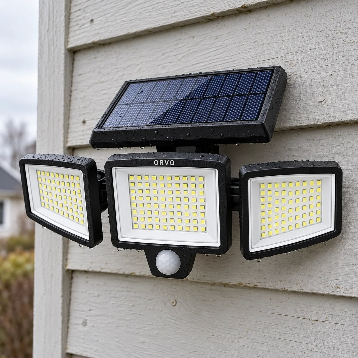 Applique solaire Orvo aux trois têtes allumées au-dessus d’une porte de garage au crépuscule, un homme rentre son vélo