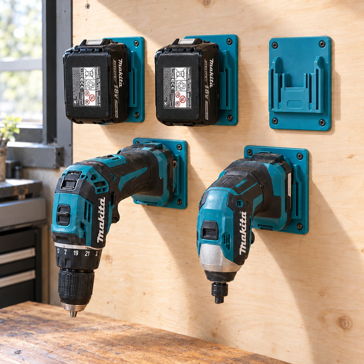 Supports turquoise sur un mur en contreplaqué avec deux batteries Makita 18V, une perceuse-visseuse, une visseuse à chocs et un support vide