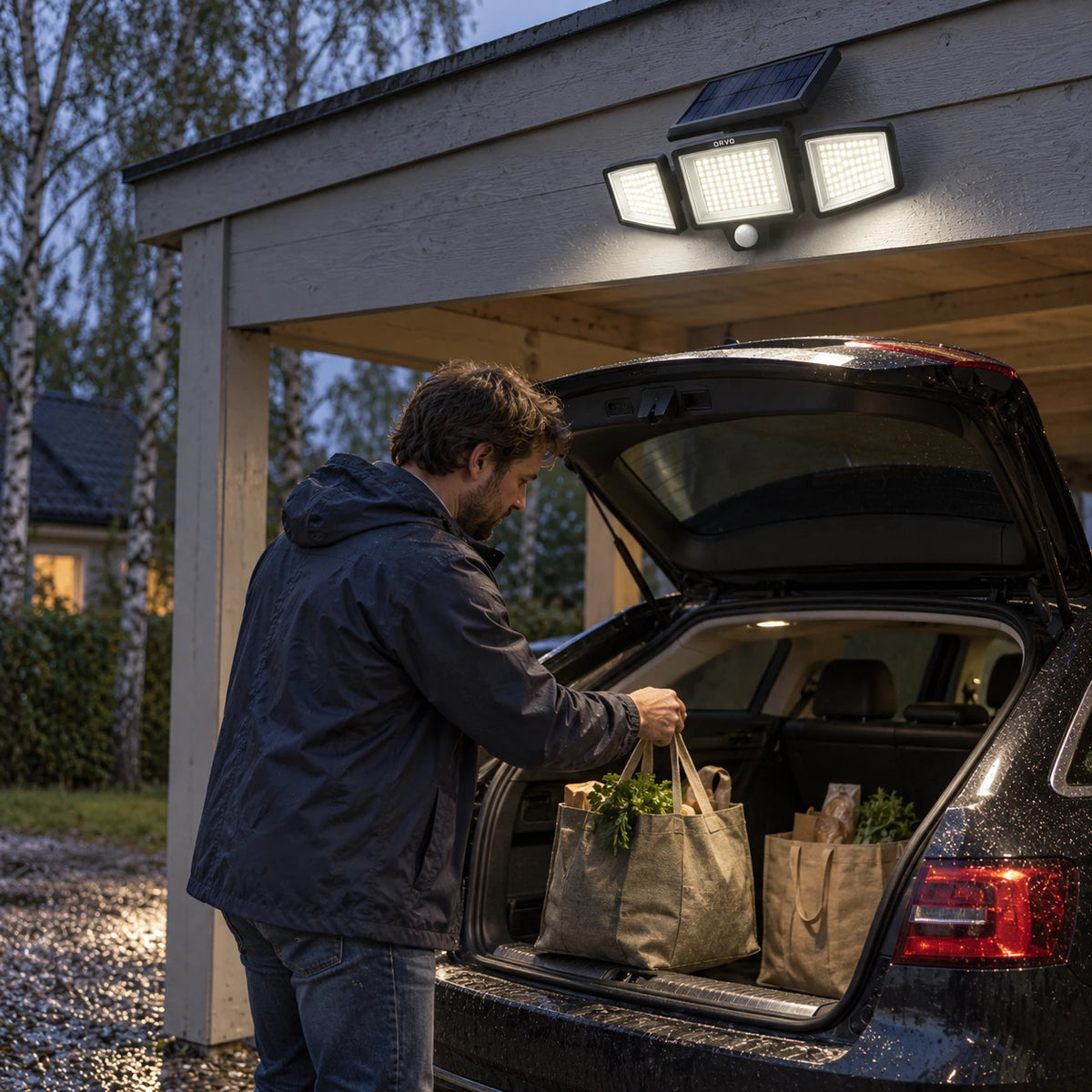 Un homme rentre son vélo dans le garage sous une applique solaire Orvo allumée, par un sombre soir d’automne